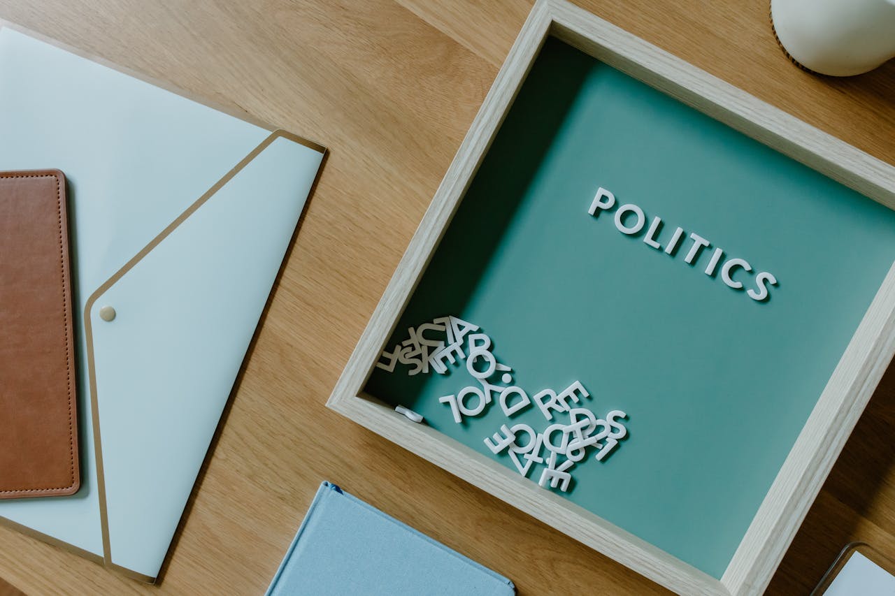 About Top view of a box with 'POLITICS' text alongside office items on a wooden desk.